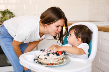Happy mother with one year old baby celebrating with first birthday with white kitchen on background
