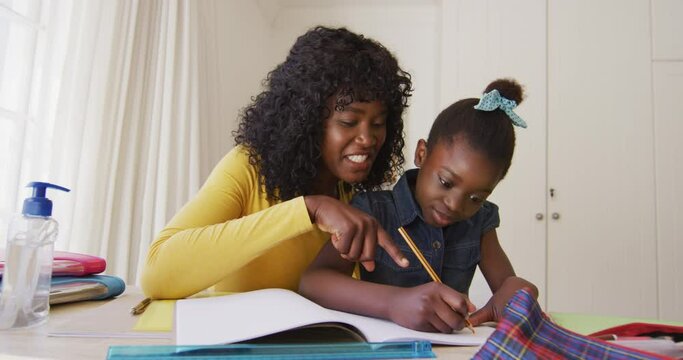 African american mother helping daughter with homework while sitting at home