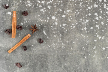 Cinnamon sticks and raisins on a dark background with falling snow.