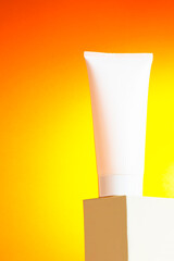 White plastic tube with face cream on geometric podium. Gradient yellow orange background. Mockup