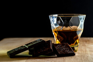 A glass of brandy. Whiskey. Cognac with dark chocolate pieces on wooden table and Black Background