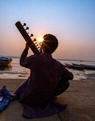 a man playing sitar at bank of ganges river at varanasi and beautiful sunrise