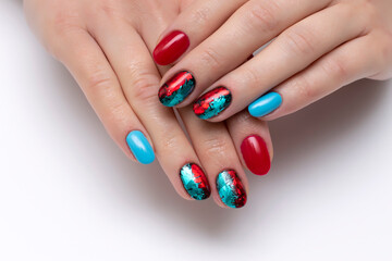 Red, blue manicure with shimmery foil on short oval nails close-up on a white background