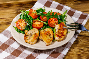 Fried chicken breast with salad of fresh arugula and cherry tomatoes on wooden table