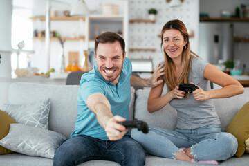Husband and wife playing video game with joysticks in living room. Loving couple are playing video games at home