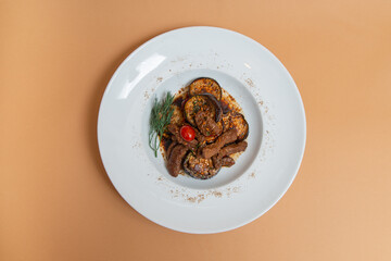 warm salad of eggplant and meat on white plate. beige background. flat lay. top view.