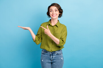 Fototapeta na wymiar Photo of pretty cute lady short hairstyle funny interested look directing finger hold hand empty space wear denim jeans green shirt isolated blue color background