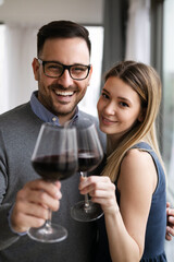 Cheerful beautiful young couple hugging and drinking red wine at home