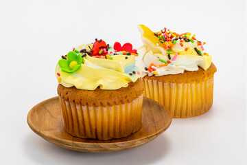 Vanilla cupcake garnished with vanilla butter cream frosting and multicolored sprinkles in wooden plate on white background with clipping path.