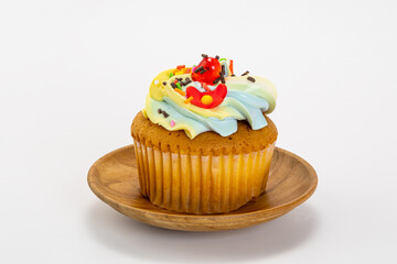 Single vanilla cupcake with butter cream frosting decorate with multicolored sprinkles in a wooden plate isolated on white background with clipping path.