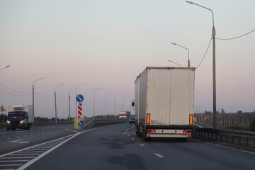 European van truck with white semi trailer drive on two lane suburban asphalted empty highway road, back view at summer evening on clear sky background, transportation cargo logistics