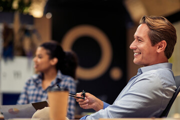 Happy cheerful mature businessman holding eyeglasses and smiling while working with colleagues in the modern office