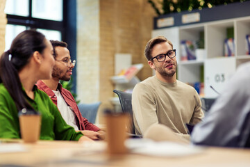 Young male office worker discussing something with multiracial colleagues while working together in the modern office