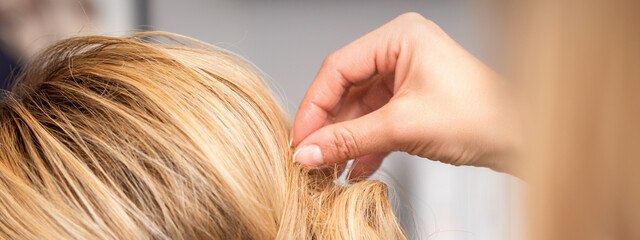 Close up back view of hand of female hairdresser makes hairstyle of young blonde woman in beauty salon