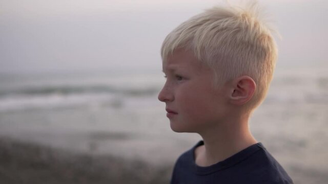 A close-up of the face on the side of a beautiful blonde boy in the evening by the sea.
