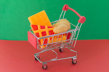 Shopping basket on a red and green background with plastic pizza, croissants and waffles inside....