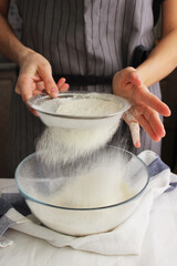 Household. A woman's hands sift flour with a sieve over a large bowl for making homemade cakes.