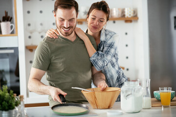  Husband and wife making pancakes at home. Loving couple having fun while cooking.