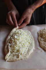 Household. Women's hands form dough sprinkled with cheese for making khachapuri. Family celebration.