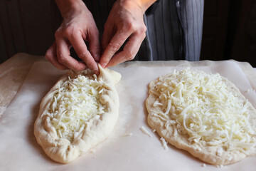 Household. Women's hands form dough sprinkled with cheese for making khachapuri. Family celebration.