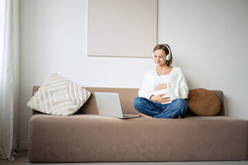 Pregnant woman uses laptop and listening to music in headphones  