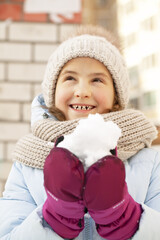 Winter portrait of a happy beautiful girl in a winter knitted hat. Girl holding snow. Vertical shot. Lifestyle