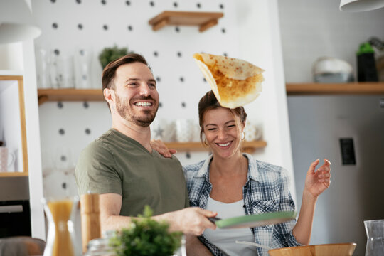  Husband and wife making pancakes at home. Loving couple having fun while cooking.