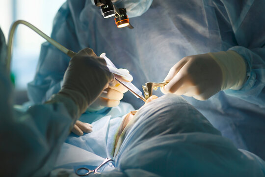 Surgeon and his assistant performing cosmetic surgery on nose in hospital operating room. 