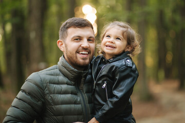Portrait of beautiful little girl with her dad. Happy daughter on fathers hands in autumn forest. Two year girl