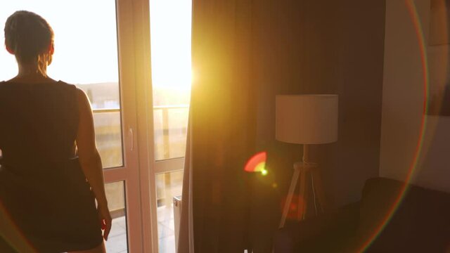 Woman opens curtains to let sunlight into the room