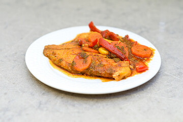 Fish in hot tomato sauce with vegetables on white plate. Homemade tasty food ready to eat.