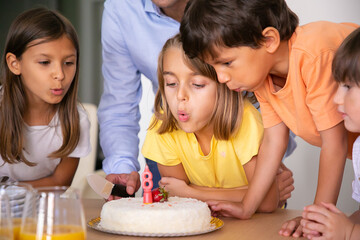 Lovely kids blowing out candle and making wish. Blonde Caucasian girl celebrating her birthday with friends and cake. Happy children having fun together. Childhood, celebration and holiday concept