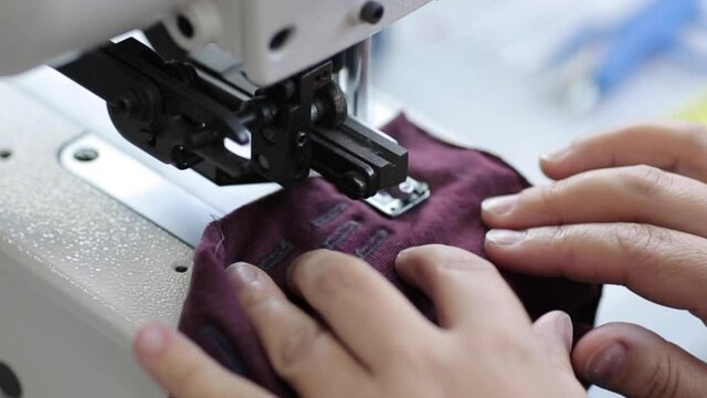The worker is sewing a textile with a sewing machine in a fabric factory.