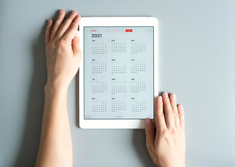 a tablet with an open calendar for 2021 year in a womans hands on a gray background