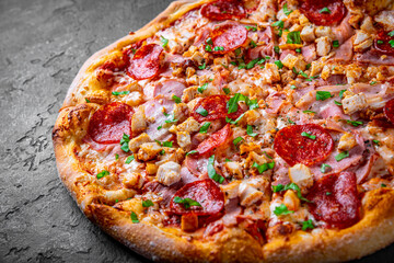Pizza with Mozzarella cheese, salami, chicken meat, bacon, ham, Tomato sauce, pepper, spices. Italian pizza on Dark grey black slate background