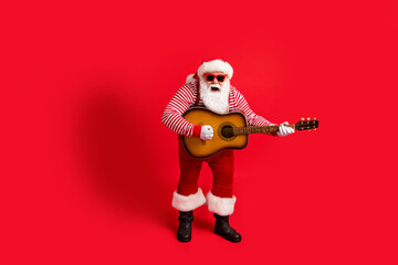 Fototapeta na wymiar Full length photo of retired old man play guitar open mouth sing performance wear santa costume suspenders sunglass striped shirt headwear boots isolated red color background