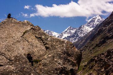 Snow capped Himalayan mountains rising beyond a large rocky boulder capped with a small Buddhist stone stupa.