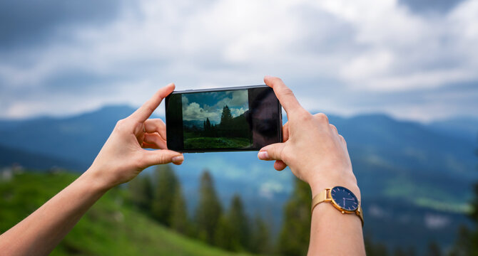 Young woman using smart phone camera for making picture of Swiss Alps. Female traveler blogger taking photos on mobile phone during summer journey vacations.