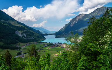 Naklejka na ściany i meble Panoramic view of idyllic scenery of Lake Lungern with fresh green meadows. Beautiful sunny day in springtime in Switzerland. Summer rural view. Village in green mountain valley.