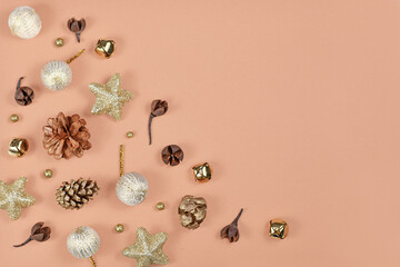 Christmas flat lay with golden fir cones, dried plant parts, bells and tree ornament baubles in corner of light brown background with empty copy space