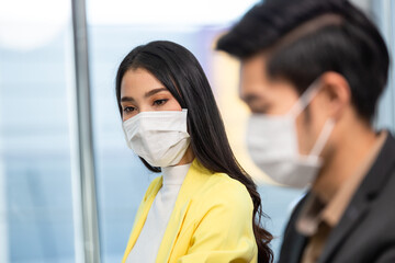 Fototapeta na wymiar Asian employee woman in face mask watching colleague working at desk. new normal people adaptation in office. business company reopen concept
