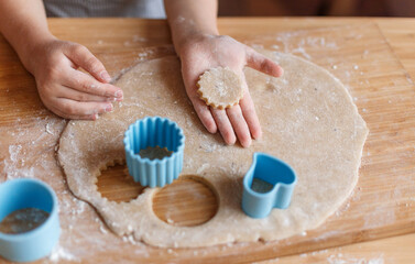 Children's hands make New Year's gingerbread cookies on a wooden table. Making cookies with a cookie cutter. New Year and Christmas concept.