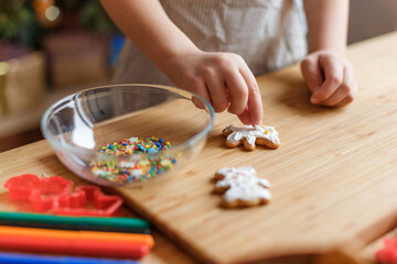 The child decorates New Year's gingerbread cookies on a wooden table. New Year and Christmas concept.