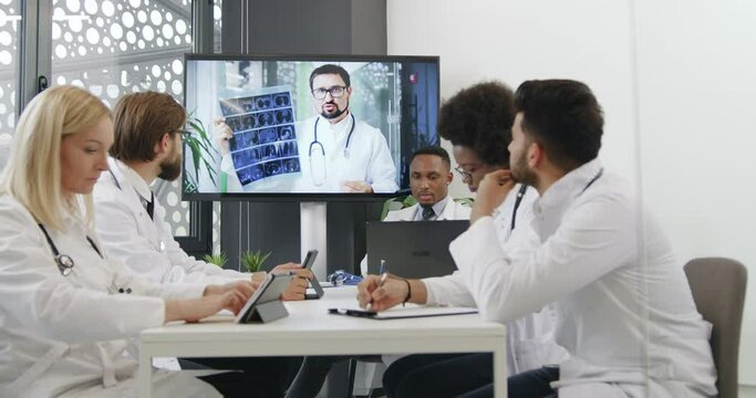 Front view of high-skilled good-looking concentrated mixed race medical team which listening video presentation on digital whiteboard in office room