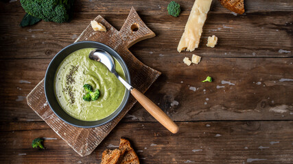 bowl of broccoli cream soup with parmesan cheese and crunchy croutons on wooden table, top view