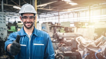 Confident engineer in blue jumpsuit with hard hat giving thumbs up in the warehouse.	
