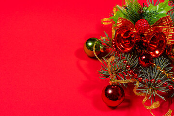 A branch of the Christmas tree with balls and bells on the red background layout. Copy space.