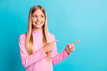 Photo portrait of curious girl pointing with finger showing looking at copyspace isolated on vibrant teal color background