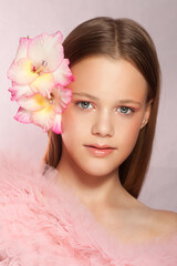 Young beautiful woman with perfect skin and a flower in her hair on pink background