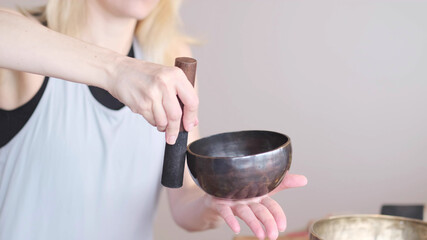 Woman playing on Tibetan singing bowl while sitting on yoga mat. Vintage tonned.
